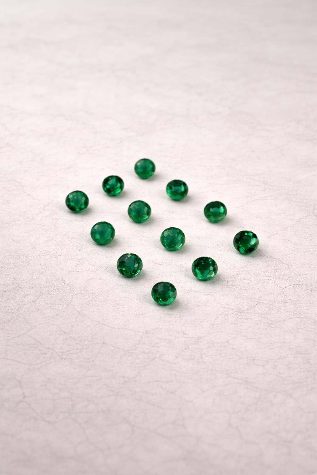 Twelve round faceted green gemstones arranged in a diamond pattern on a light textured surface.