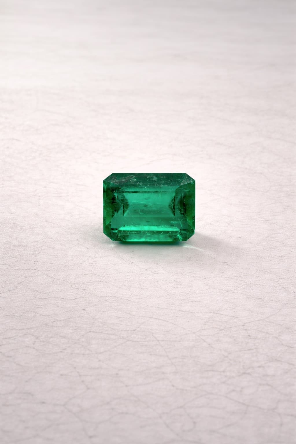 A vibrant green emerald-cut gemstone centered on a light-colored, textured surface with soft shadows.